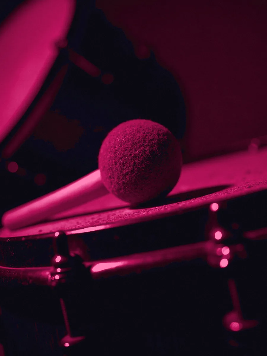 A felt beater resting against a bass drum head under a magenta gel, the shell falling out of focus into the dark behind