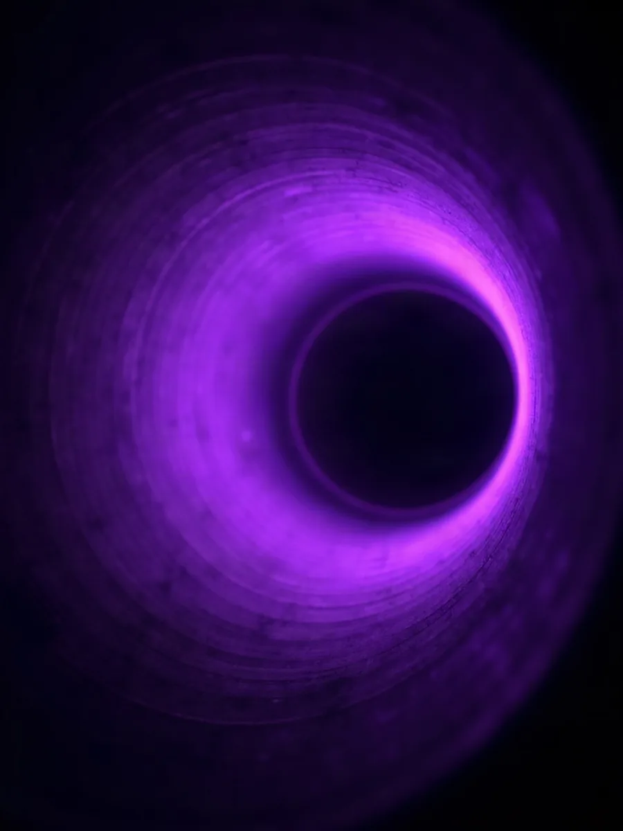 Looking into the mouth of a large resonating tube, a violet gel ringing the rim and the bore going black